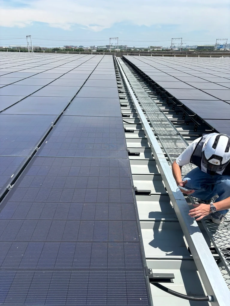 Genuine rooftop solar photograph with restrained exposure and color adjustment, showing modules and a field worker; the specific site is unconfirmed.